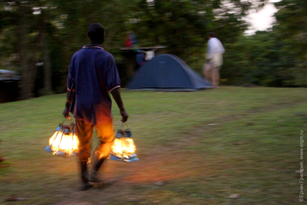 Служитель кемпинга разносит керосиновые лампы Африка Уганда