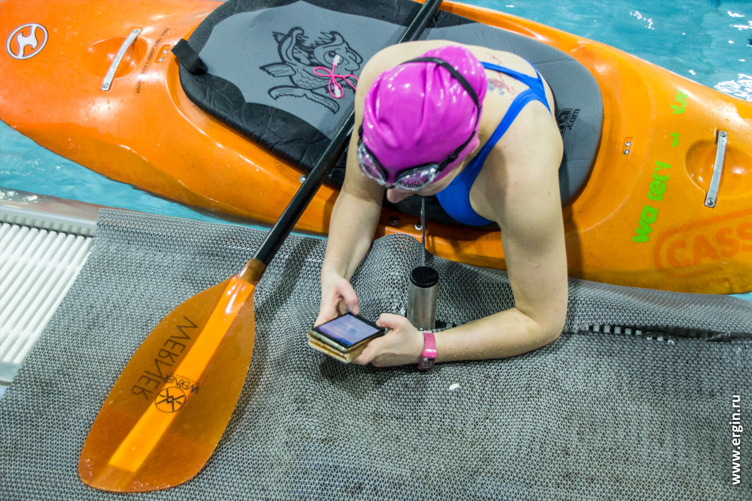 Каякер в бассейне сидя в воде набирает на смартфоне сообщение